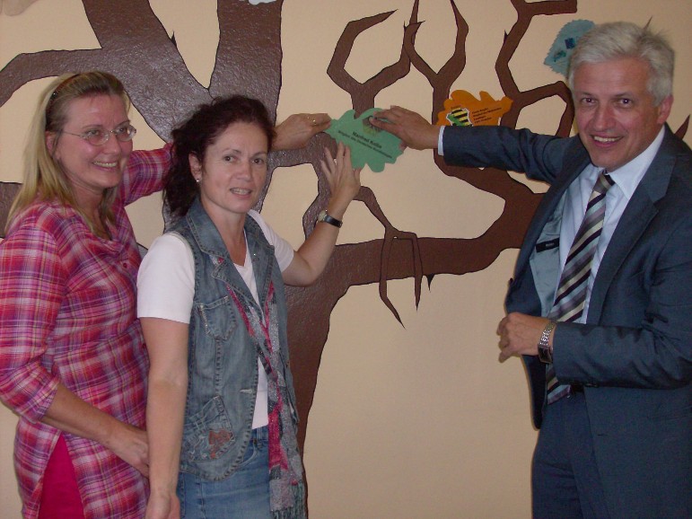 Ulrike Brucks, Sybille Zugowski und Manfred Kolbe kleben das Patenblatt an den Patenbaum des MGH Dommitzsch